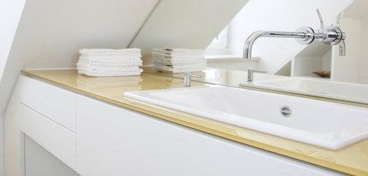 Der Waschtisch des Gäste-WCs besteht aus einer rückseitig lackierten Glasplatte, in die ein Handwaschbecken eingelassen ist, die Wandarmatur ist durch den rückseitigen Spiegel geführt.