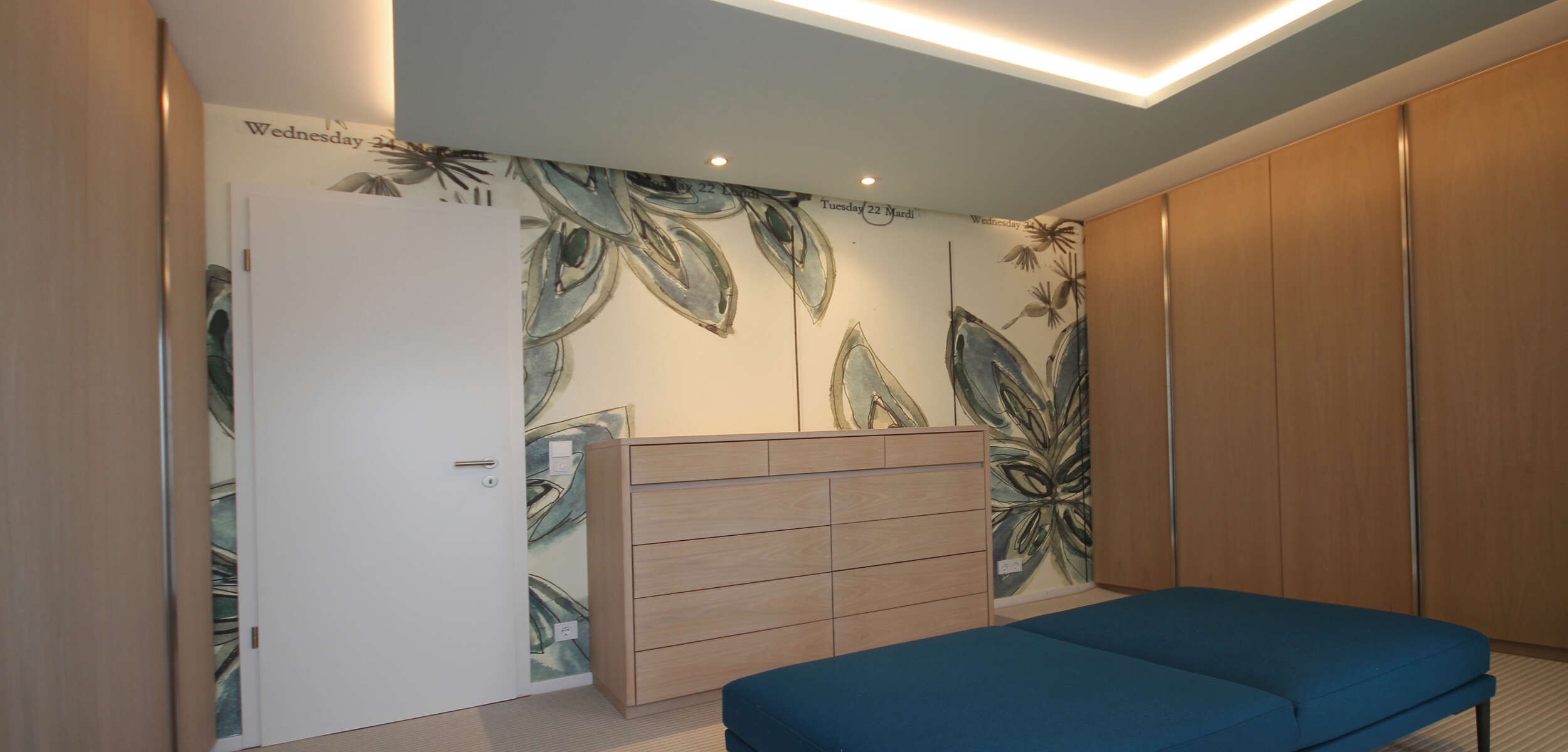 Elegantes Ankleidezimmer mit trendiger Tapete, moderner Wäschekommode und schicker Sitzbank, gestaltet von einem Innenarchitekten in München.