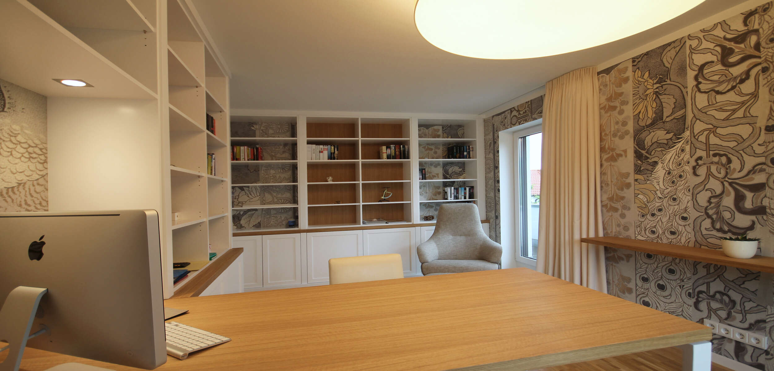 Modern eingerichtetes Arbeitszimmer mit hölzernem Schreibtisch, bequemem Lesesessel und stilvollem Einbauschrank durch einen Innenarchitekten aus München.
