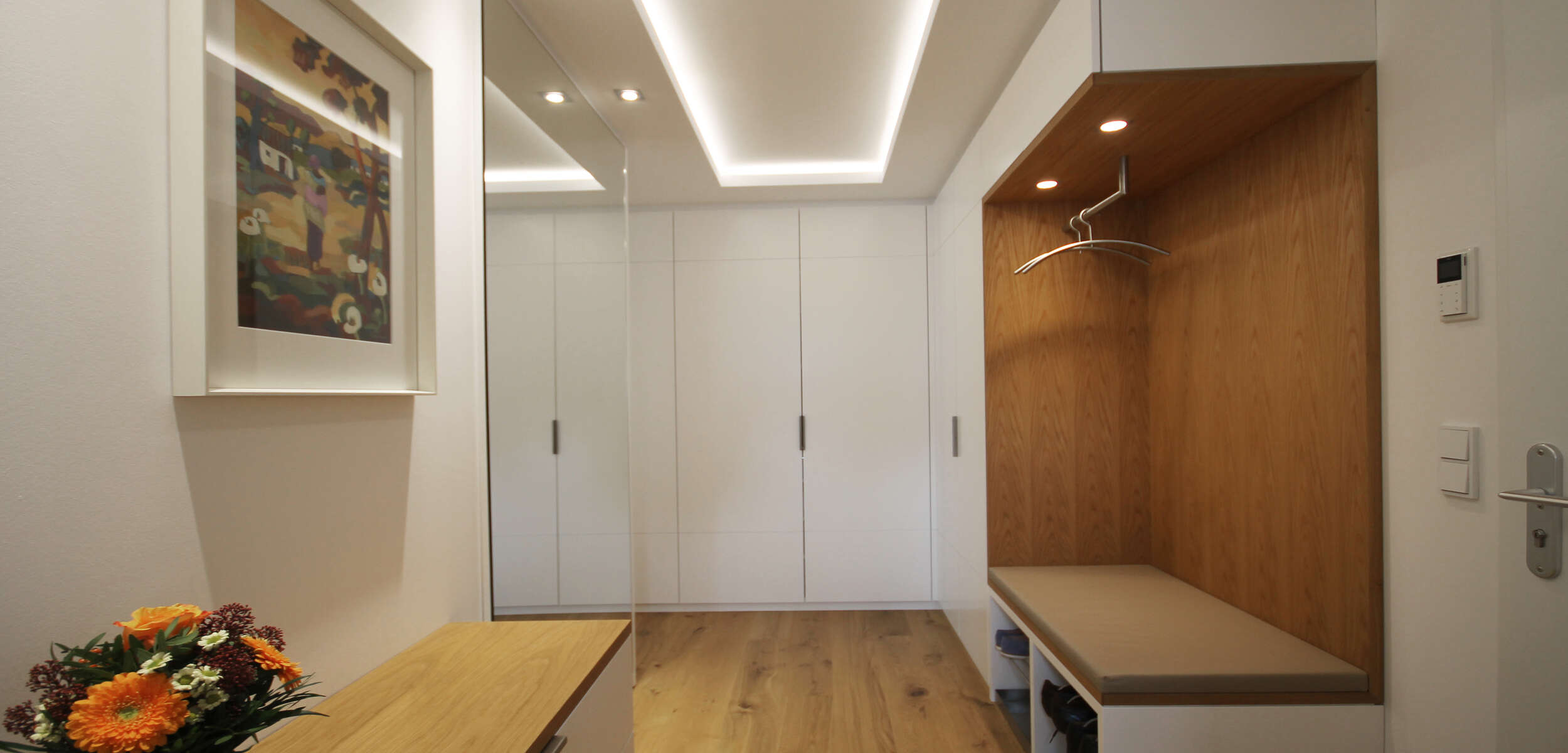 Eleganter Eingangsbereich mit Holzdielenboden, moderner Gaderobe und stilvoll eingerichtetem Sitzbereich durch Münchener Innenarchitekten.