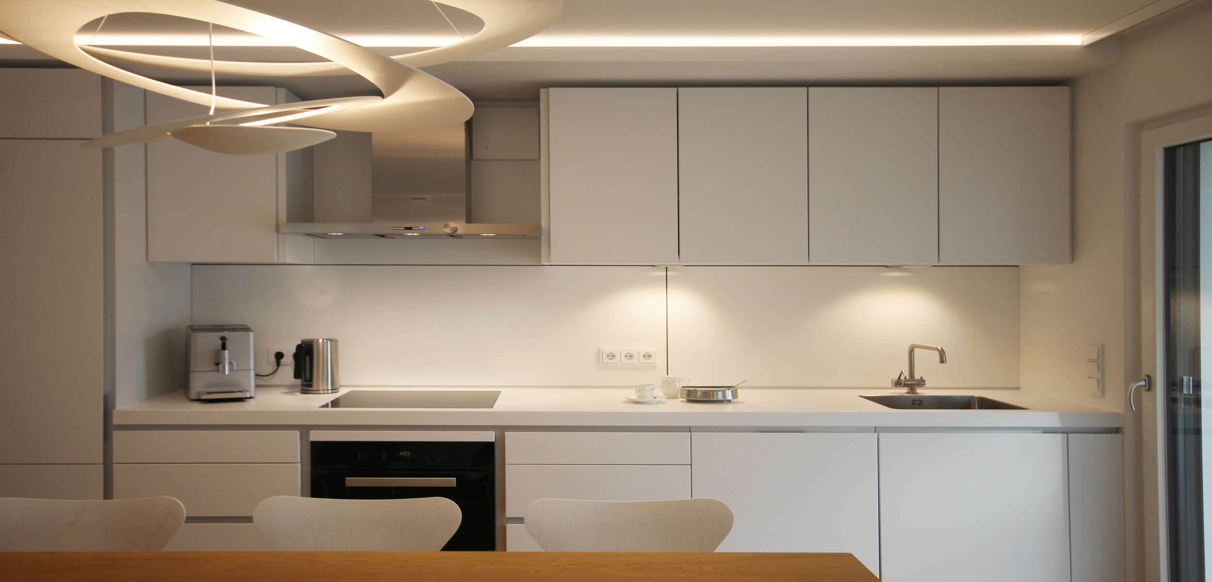 Schlichtes und elegantes Interior Design einer Küche mit moderner Küchenzeile und hängenden Schränken in hellem Holz.