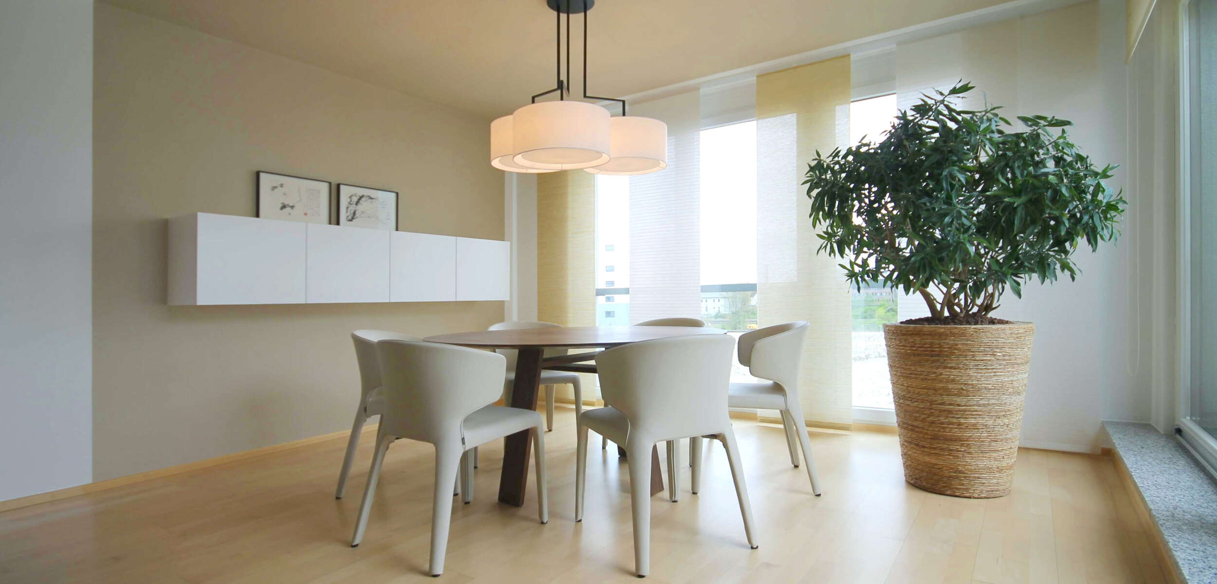 Modernes, minimalistisches Speisezimmer-Design mit einem langen Holztisch, umgeben von 8 Stühlen, hängender Beleuchtung und einer Wand mit Bücherregalen.