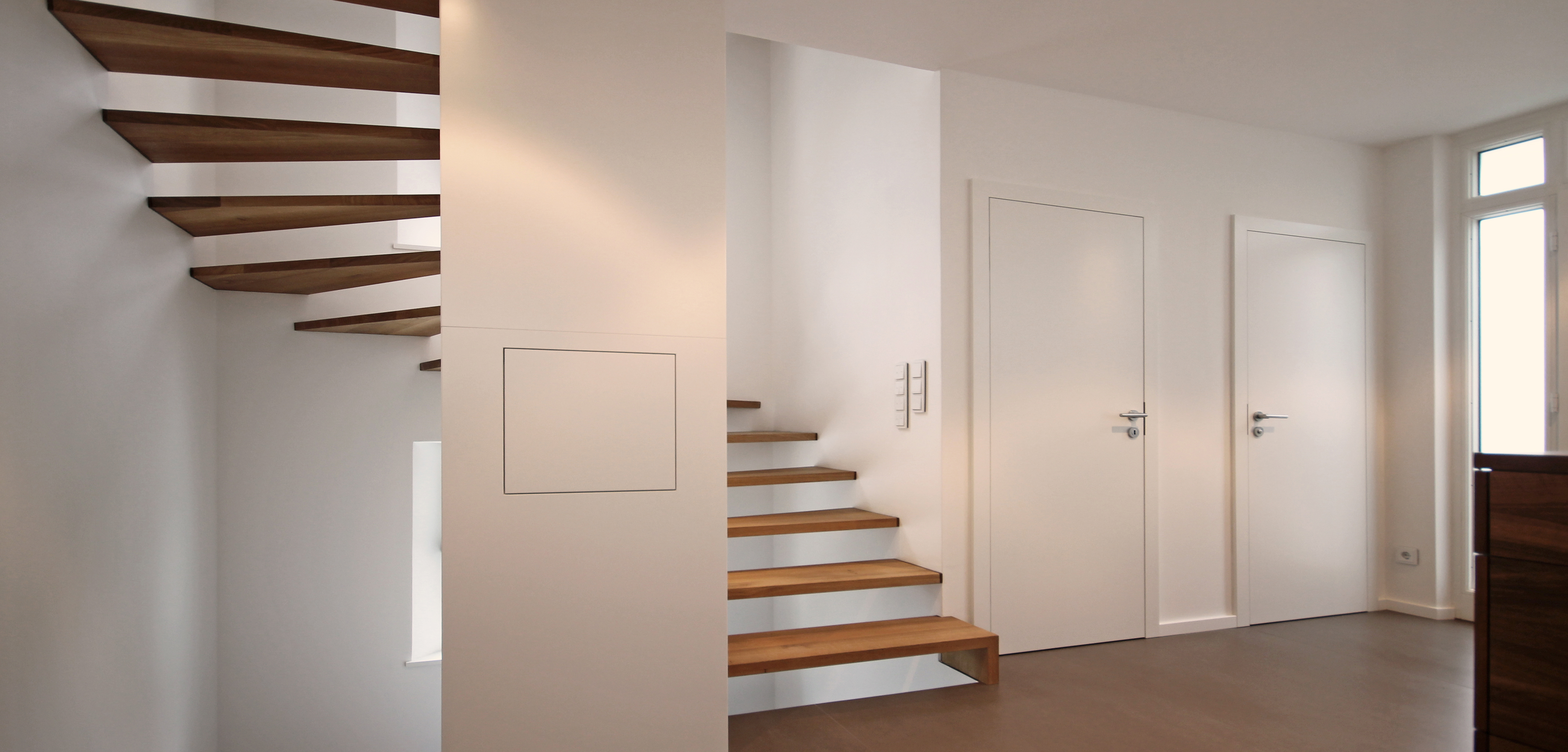 Innenansicht eines modern umgebauten Einfamilienhauses: eine helle Holztreppe mit weißen Wänden und klarer Linienführung.