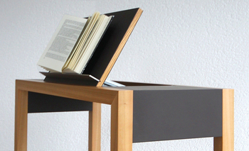 Der Lesetisch kann auch als Konsole genutzt werden. Die bündig eingelassene Buchstütze wird bei Bedarf ausgeklappt und der Lesetisch über das Sitzmöbel geschoben.