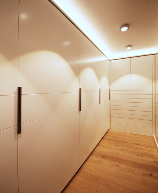 Die flächenbündigen Schiebetüren des Kleiderschranks sind weiß lackiert, beim Öffnen der Türen wird automatisch die Innenbeleuchtung eingeschaltet.