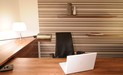 Der Arbeitsbereich mit Schreibtisch, Sideboard, Container aus Nussbaum wird durch eine Tapete mit Streifen betont. Bürostuhl aus Leder, Wandboard, Tischleuchte.