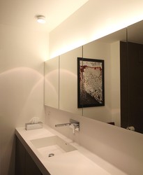 Der Spiegelschrank trägt eine indirekte Beleuchtung als Ergänzung für die Deckenstrahler, die als Aufbauleuchten an der Rohdecke montiert sind, Kabel laufen im Deckenputz.
