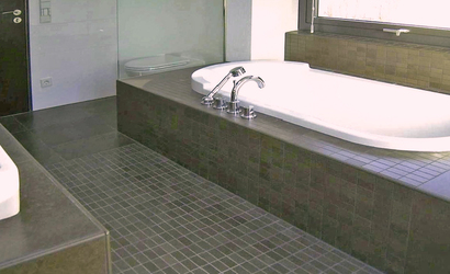 Ein Teppich aus Mosaikfliesen verbindet Waschtisch und Badewanne über den Boden. Die Fensterbank wird gleichzeitig als Ablagefläche für die Wanne genutzt.