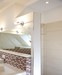 Die ebenerdige Dusche kommt ohne Duschtasse aus und wird nur durch eine halbhohe Trennwand vom Raum abgegrenzt. Ein Winkel mit buntem Mosaik schafft Atmosphäre.
