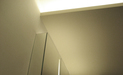 Eine Abhangdecke ist über einen Teilbereich des Raumes geführt, in der Deckenkante ist eine Lichtvoute als dimmbare indirekte Beleuchtung mit warmer Lichtfarbe eingebaut.