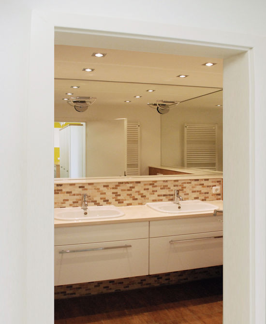 Wandleuchten sind direkt auf den Spiegel montiert und sorgen für eine brilliante Ausleuchtung des Waschtisches. Downlights in der Abhangdecke schaffen die Grundbeleuchtung.