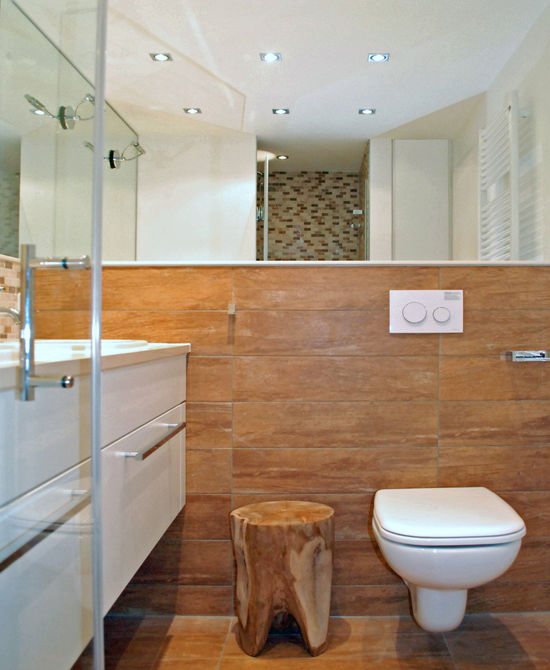 Die Duschkabine ist durch eine rahmenlose Ganzglastür geschlossen, die Oberflächen sind mit Mosaikfliesen belegt, die Armaturen sind als Regen-Kopfbrause und Handbrause ausgeführt.