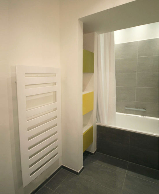 Die Regalnische wurde in Trockenbau erstellt und grenzt die Badewanne ab. Eingeschobene Schrankkorpen sind mit Drehtüren versehen, die in Gelb- und Grüntönen lackiert sind.
