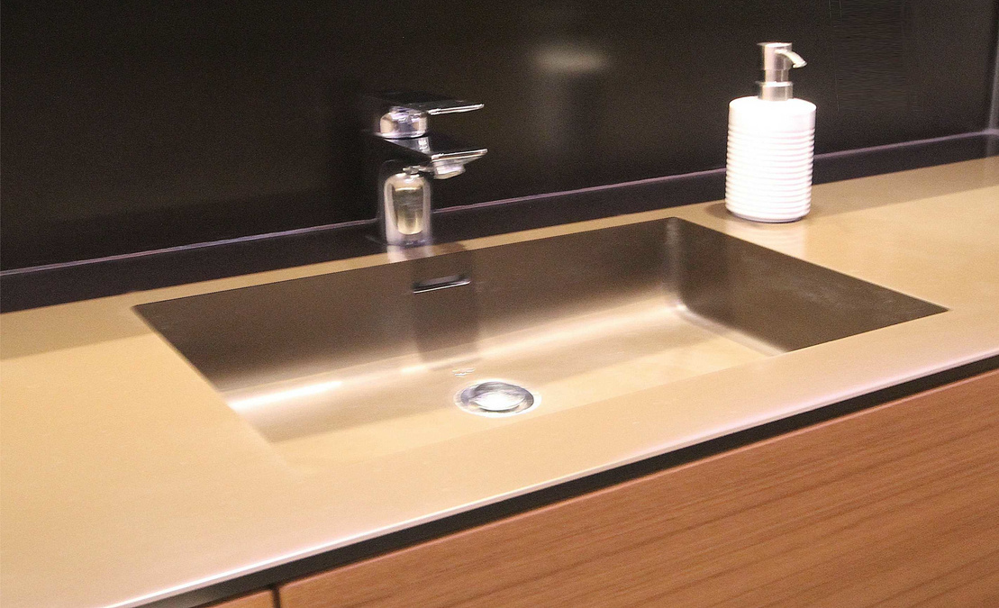 Das Waschbecken besteht aus demselben Material Corian wie die Waschtischplatte und ist fugenlos in die Fläche integriert, der kaffeebraune Farbton passt zum Holzfurnier.