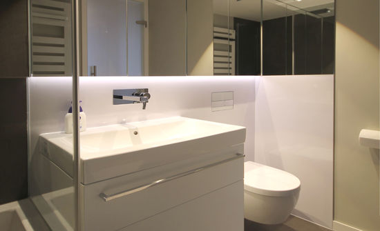 Die Fronten des Waschtisches und der Rückwand des Hänge-WC sind aus HPL mit Hochglanzoberfläche gefertigt, eine Glaswand trennt Waschtisch und Badewanne voneinander ab.