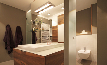 Der Waschtisch des Badezimmers ist mittig im Raum platziert und trennt die Duschkabine vom WC-Bereich mit Bidet, ein raumhoher Spiegel weitet optisch die Größe des Raumes.
