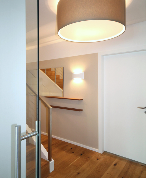 Ein Spiegelpaneel weitet den schmalen Flurbereich. Die transparente Glasschiebetür grenzt Diele und Wohnraum ab, erzeugt aber optisch einen fließenden Übergang der beiden Räume.