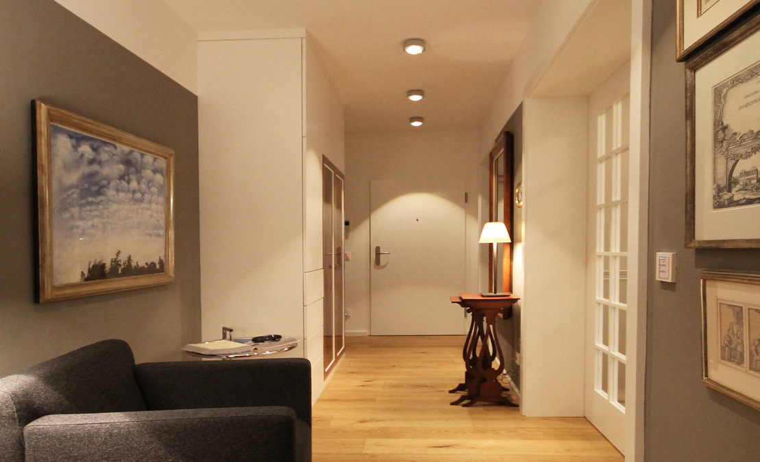 Die Diele bringt im Bereich der Wohnungseingangstür die Garderobe und einen Spiegel unter, im hinteren Bereich folgt ein Sitzbereich mit Sessel und Beistelltisch.