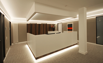 Moderne Empfangstheke in klarem Design mit beleuchtetem Logo, gestaltet durch professionelle Innenarchitekten aus München.