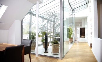 Ein Glasdach führt in den Wohnbereich, versorgt das Dachgeschoss mit Licht. Der Wintergarten trennt Wohn- und Speisebereich, ist Lebensraum unter freiem Himmel.