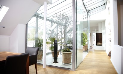 Ein Glasdach führt in den Wohnbereich, versorgt das Dachgeschoss mit Licht. Der Wintergarten trennt Wohn- und Speisebereich, ist Lebensraum unter freiem Himmel.