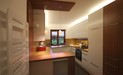 Küchenfronten zeigen weiße Lackoberflächen, Arbeitsplatten bestehen aus Resopal mit Holzoptik, die großformatigen Fliesen aus Feinsteinzeug erinnern an Basalt.