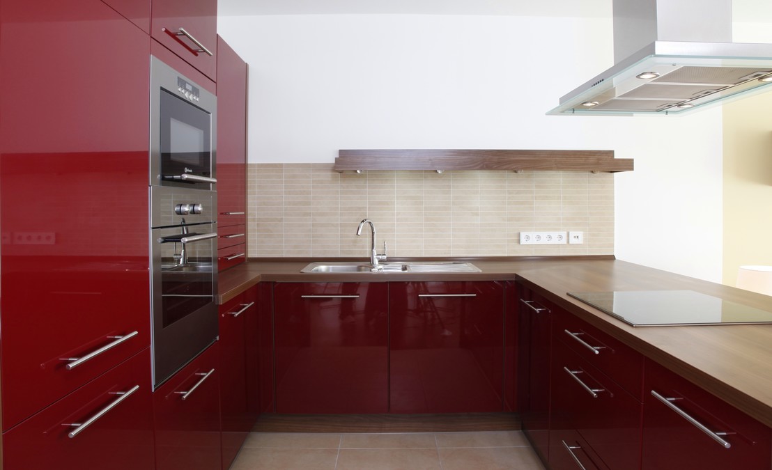 Die WohnkÃ¼che trÃ¤gt bordeauxfarbene Fronten in Hochglanzlack und Arbeitsplatten in Nussbaum. Wandfliesen passen als Mosaik zu den groÃformatigen Bodenfliesen.