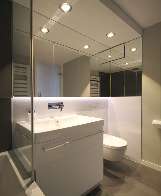 Eine Glasscheibe trennt Badewanne und Waschtisch, der Spiegelschrank schafft einen großzügigen Raumeindruck, Deckenleuchten sorgen für eine warme Beleuchtung.