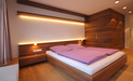 Das Schlafzimmer ist mit Oberflächen aus Nussbaum gestaltet, direktes und indirektes Licht in den Einbauten schaffen eine warme Atmosphäre, der Kleiderschrank ist teilweise begehbar.