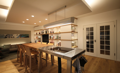 Zentrales Möbelstück in der Wohnküche ist ein langer Tisch in Form einer Werkbank, er bringt den Esstisch und die Arbeitsfläche der Küche mit einem Kochfeld unter.