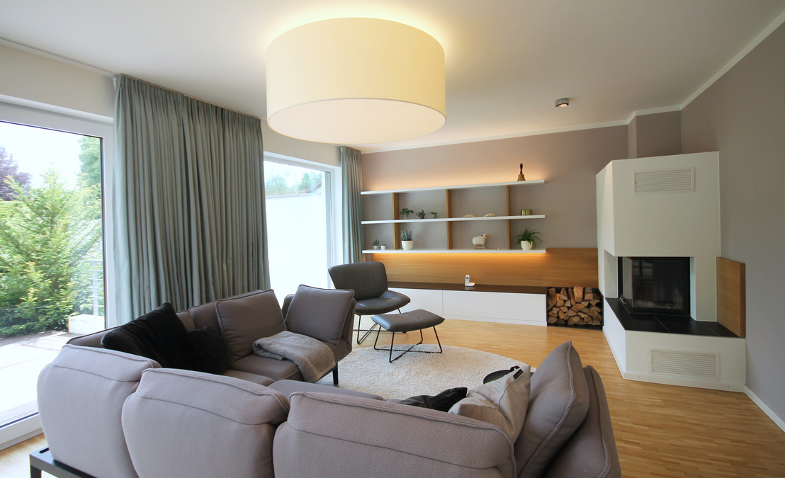 Innenarchitekt Andreas Ptatscheck, München, integrierte den Kamin mit Holzlege in die Wandgestaltung des Wohnzimmers mit Wandregal, Lowboard und Wandpaneelen aus Eichenholz.