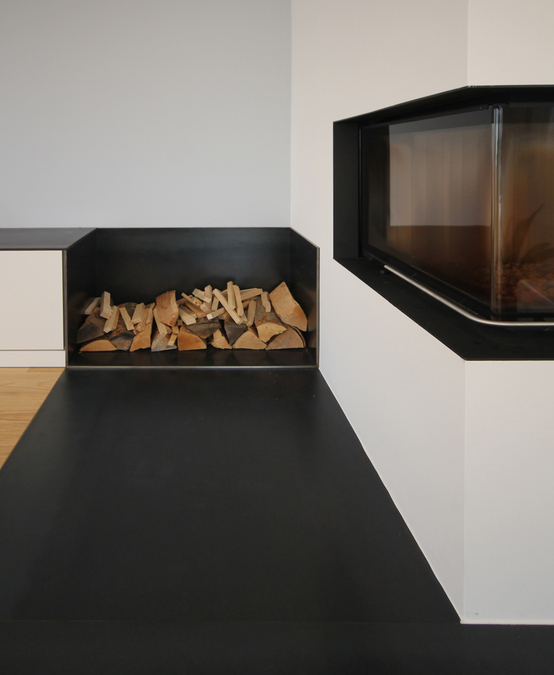 Schwarzstahl ist das verbindende Material im Kaminentwurf von Innenarchitekt Andreas Ptatscheck, München, er findet sich in der im Funkenschutz des Bodens, in der Holzlege, in der Einfassung der Feuerstelle sowie auf dem Lowboard des Schreinereinbaus.