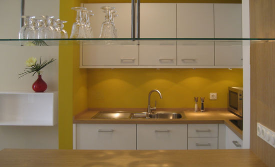 Die frei stehende Theke grenzt Wohnzimmer und Speisebereich ab und wird darin von hängenden Glasregalen unterstützt. Farbe der Küchenwand ergänzt Raumkonzept.
