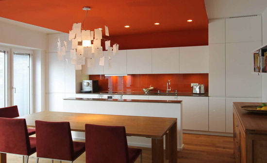 Die rostrote Abhangdecke verbindet Küche und Speisebereich, winkelt als Wandfläche ab und geht in die Küchenzeile über. Sie nimmt den Farbton der lackierten Glasplatte der Küchenrückwand auf.