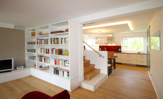 Die raumhohe Bücherwand und die dahinter liegende Treppe trennen Wohnzimmer und Küche optisch voneinander ab, dennoch besteht der Eindruck eines großzügigen Gesamtraumes.