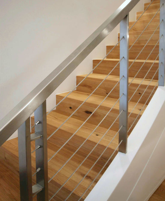 Das Treppengeländer besteht aus einem Edelstahl-Vierkantrohr mit gebürsteter Oberfläche. Die einzelnen Stützen sind durch gespannte Stahlseile elegant miteinander verbunden.