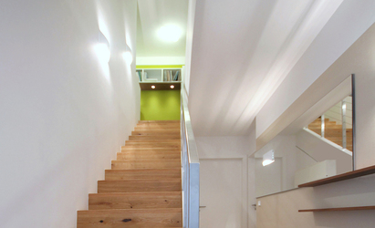 Die Treppe mit Massivholzbelag und einem Geländer aus gebürstetem Edelstahl führt ins Obergeschoss der Wohnung. Die Wandleuchten im Treppenbereich passen zu den Leuchten der Diele.