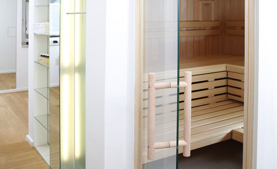 Der Wellnessraum verfügt über eine Sauna, die mit einer Verkleidung aus Gipskarton versehen ist. Das integrierte Glasregal mit Spiegelwand weitet den Durchgang.