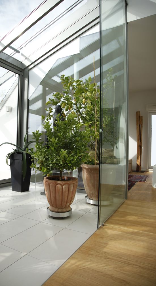 Der Wintergarten wird zum Innenraum mit rahmenlosen Glasschiebetüren geschlossen. Im Winter finden hier die Balkonpflanzen in großen Blumenkübeln ihren Platz.