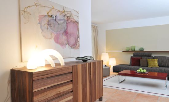 Das Sideboard aus Nussbaum Massivholz ist wertvoller Blickfang und vermittelt zwischen Wohnzimmer und Speisebereich. Darüber ein Gemälde mit floralem Motiv.