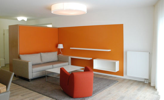 Die Anordnung der Möbel, Leuchten und Einbauten bildet einen Raum im Raum. Farben sind freundlich und anregend, sollen auch bei schlechtem Wetter heitere Atmosphäre schaffen.