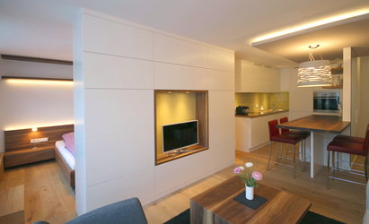 Der Wohnzimmerschrank besteht aus einzelnen Korpen mit weiß lackierten Klappen, in der Mitte ist ein offenes und beleuchtetes TV-Fach mit farbig lackierter Rückwand integriert.