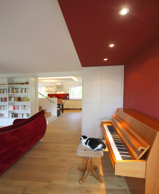Ein Farbwinkel in Wand und Decke markiert die Position des Klaviers im Wohnraum, Deckenspots sorgen für eine gute Beleuchtung, der Parkettboden läuft bis in die Küche.